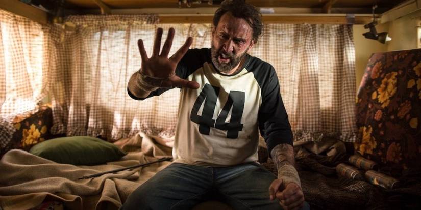 Nicolas Cage as Red sitting on a bed and holding up his hand in Mandy