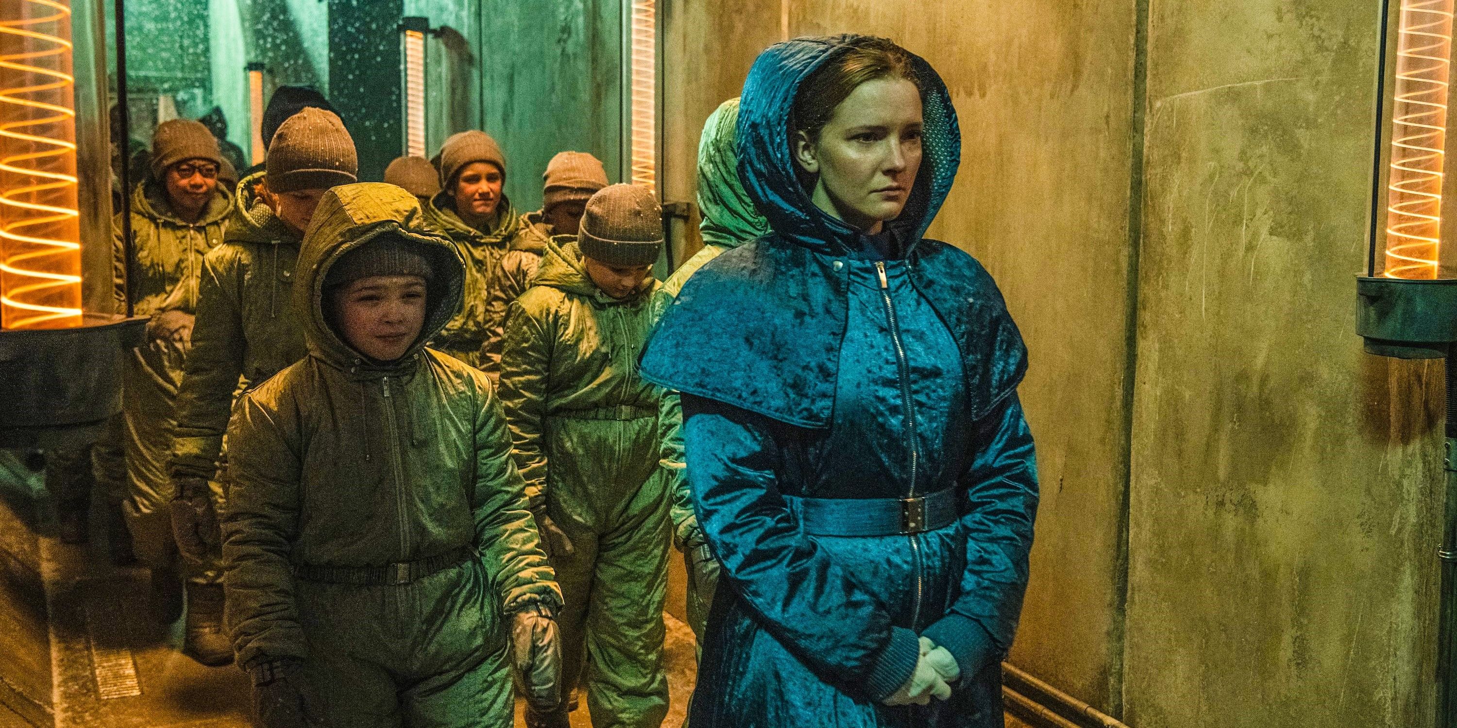 Morfydd Clark as a nurse wearing a blue jacket and leading a group of children in His Dark Materials.