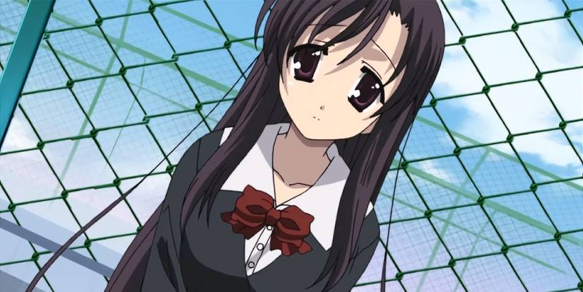 A school girl standing in front of a metal fence and looking sad in the School Days anime.