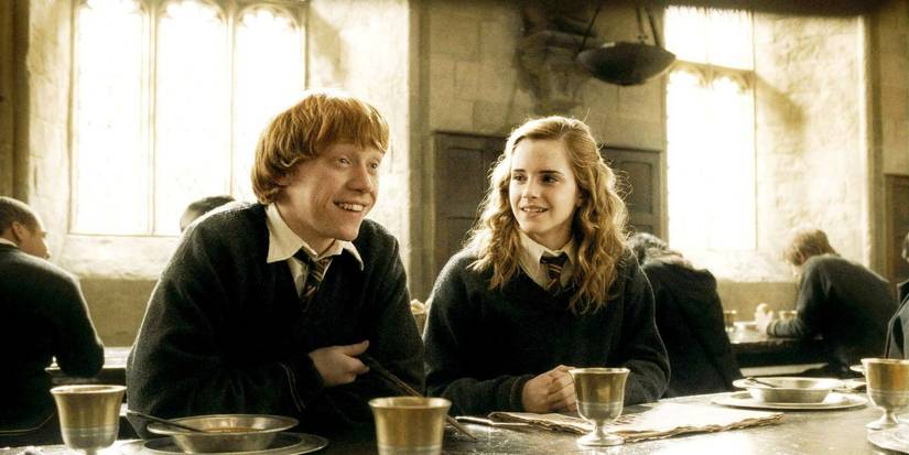 Ron Weasley (Rupert Grint) and Hermione Granger (Emma Watson) smiling in the Hogwarts Great Hall in Harry Potter. 