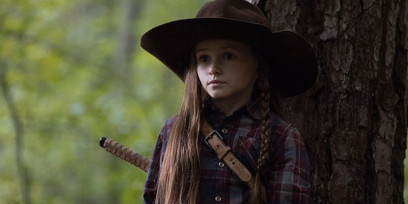 Cailey Fleming as Judith standing by a tree while wearing Rick's hat in The Walking Dead