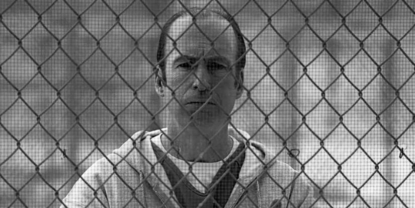 Bob Odenkirk as Jimmy McGill standing behind a chain link fence in prison in Better Call Saul 