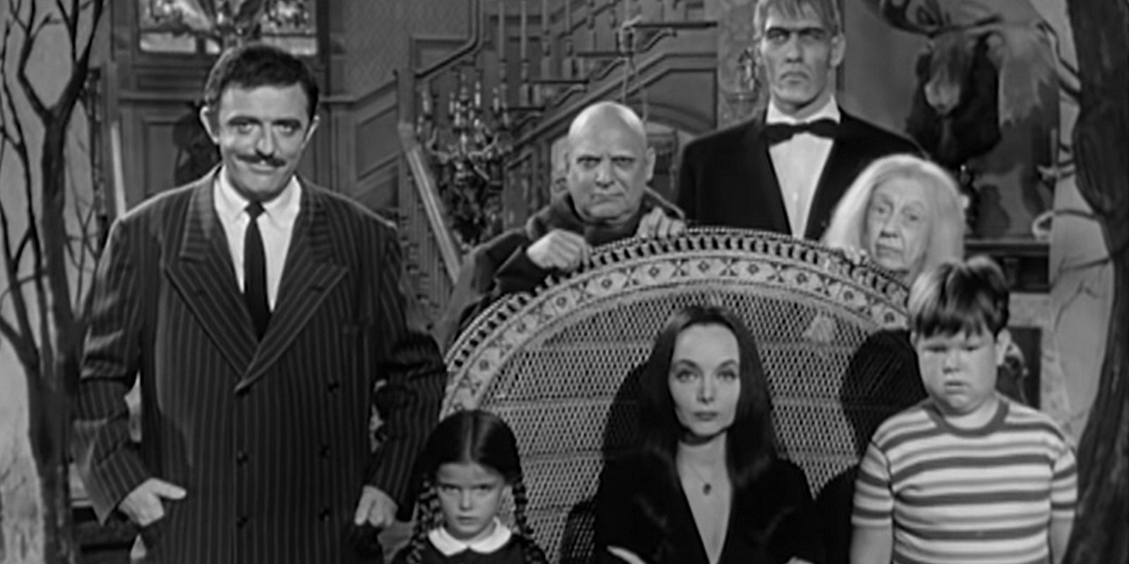 The cast of the Addams Family 1964 gathered around a chair