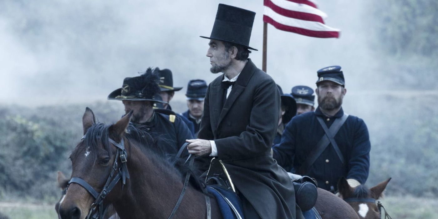 Daniel Day Lewis as Abraham Lincoln in his famous black coat and stovepipe hat sitting atop a horse, followed by mounted soldiers in Union Army uniforms carrying an American flag atop a pole
