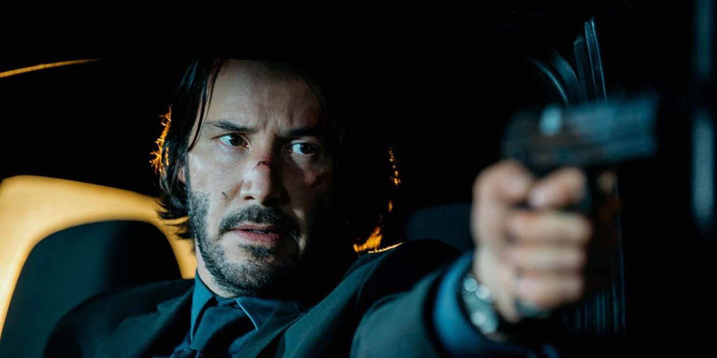 John Wick in a car, holding a gun.