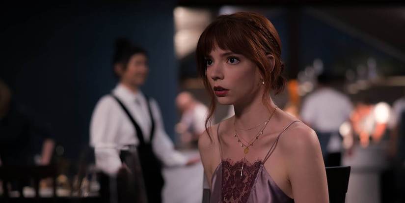 Anya Taylor Joy as Margot in The Menu waring a dress, looking terrified, servers in the background at the restaurant.
