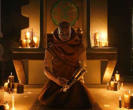 Монах из Cyberpunk 2077, склонившийся на земле рядом с несколькими горящими свечами.