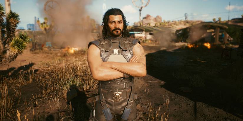 Сол из Cyberpunk 2077 стоит, скрестив руки, в лагере Альдекадо.