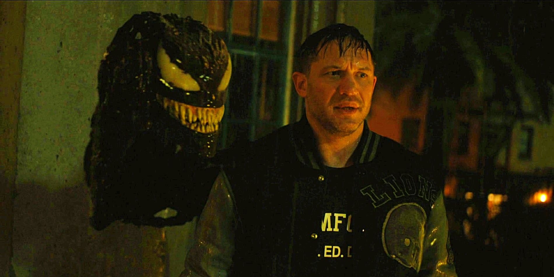 Tom Hardy in Venom Let There Be Carnage standing next to Venom's head.