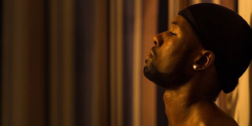 Chiron leans against a wall in an orange lit room in Moonlight