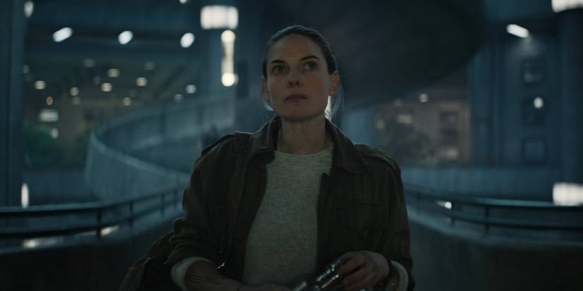 Silo's Rebecca Ferguson looking stoic with a spiral staircase behind her.