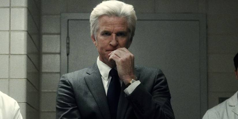 Matthew Modine como Dr. Martin Brenner, pensativo com a mão na boca em Stranger Things
