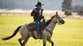 Forrie J Smith as Lloyd Pierce riding a horse and holding a gun in Yellowstone.