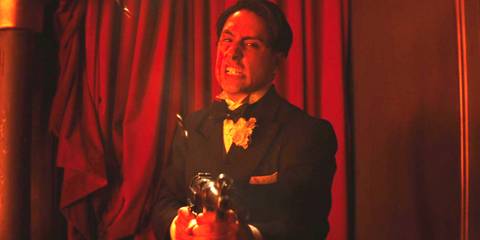 A tuxedo-wearing man with a machine gun making a furious face as he pumps bullets into someone
