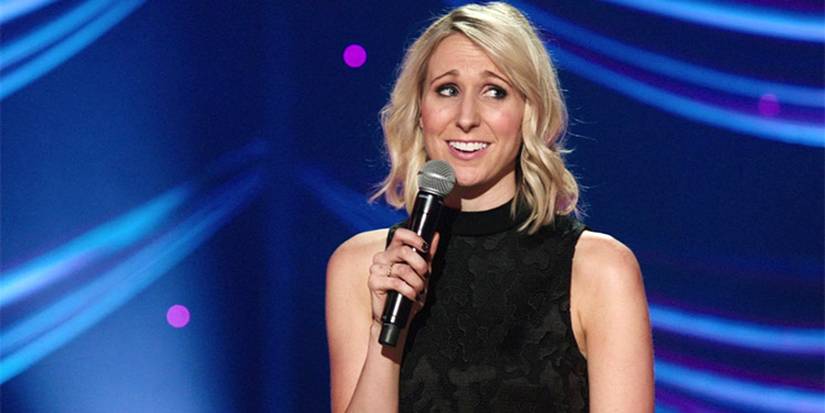 Nikki Glaser performing stand-up with a blue background