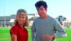 Olivia Newton-John and John Travolta smiling on the field in Grease