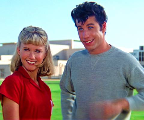 Olivia Newton-John and John Travolta smiling on the field in Grease