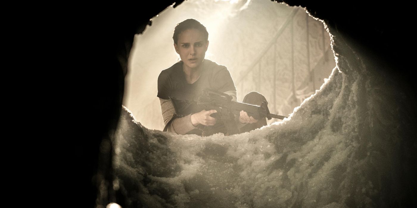 Lena holds a military weapon while looking through the entrance to a cavern.