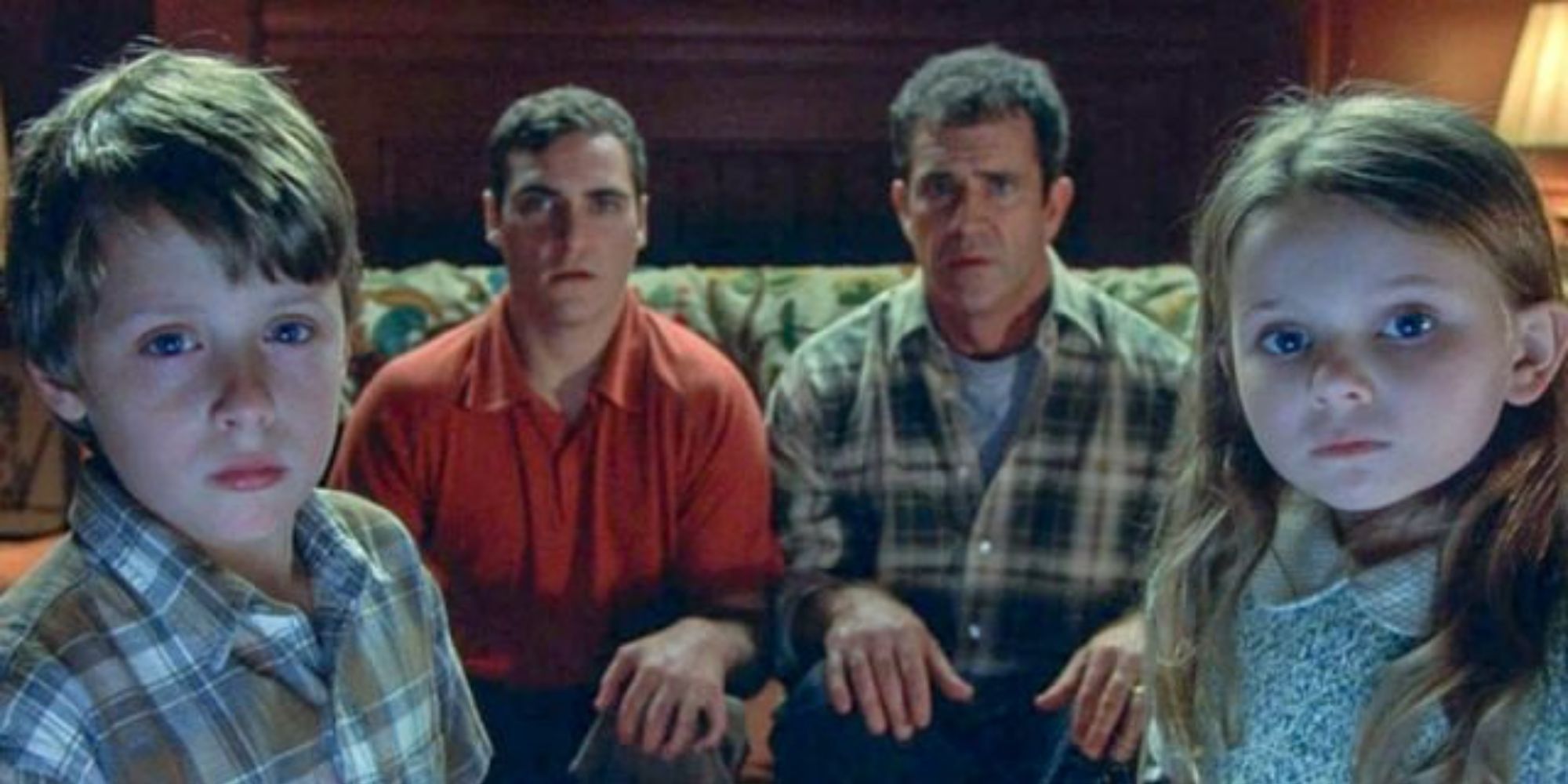 Mel Gibson's Graham, Joaquin Phoenix's Merrill, Rory Culkin's Morgan, and Abigail Breslin's Bo stare at a TV screen while sitting in Signs