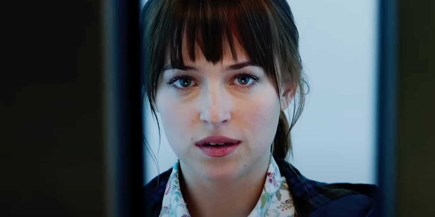Dakota Johnson as Anastasia Steele peeking through a door in 50 Shades of Grey