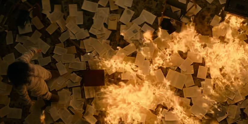 Алисия стоит перед костром, который разгорелся благодаря страницам книг.