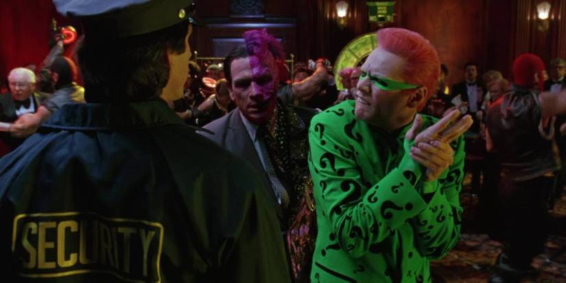 Tommy Lee Jones as Two-Face and Jim Carrey as Riddler looking at a police officer (whose back is to the camera) in Batman Forever