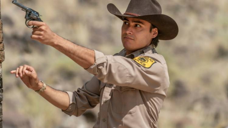 Kiowa Gordon as Jim Chee aiming his gun in Dark Winds.
