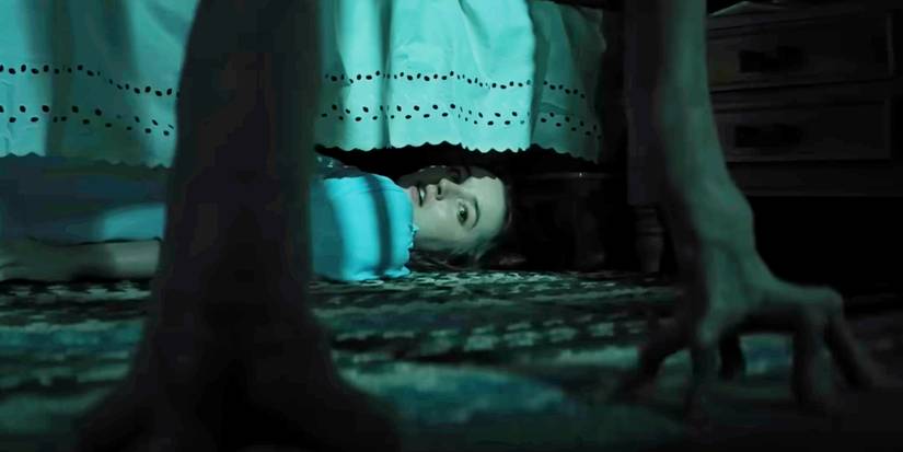 Kaitlyn Dever hides under a bed looking at two alien feet in No One Will Save You.