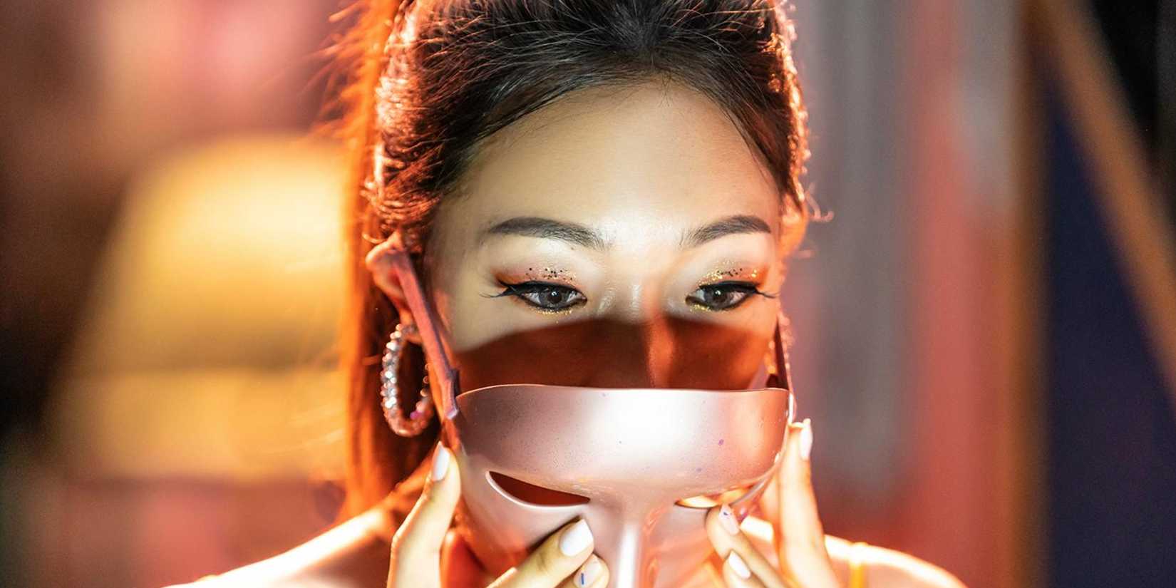 Uma mulher colocando uma máscara dourada rosa no thriller Mask Girl.