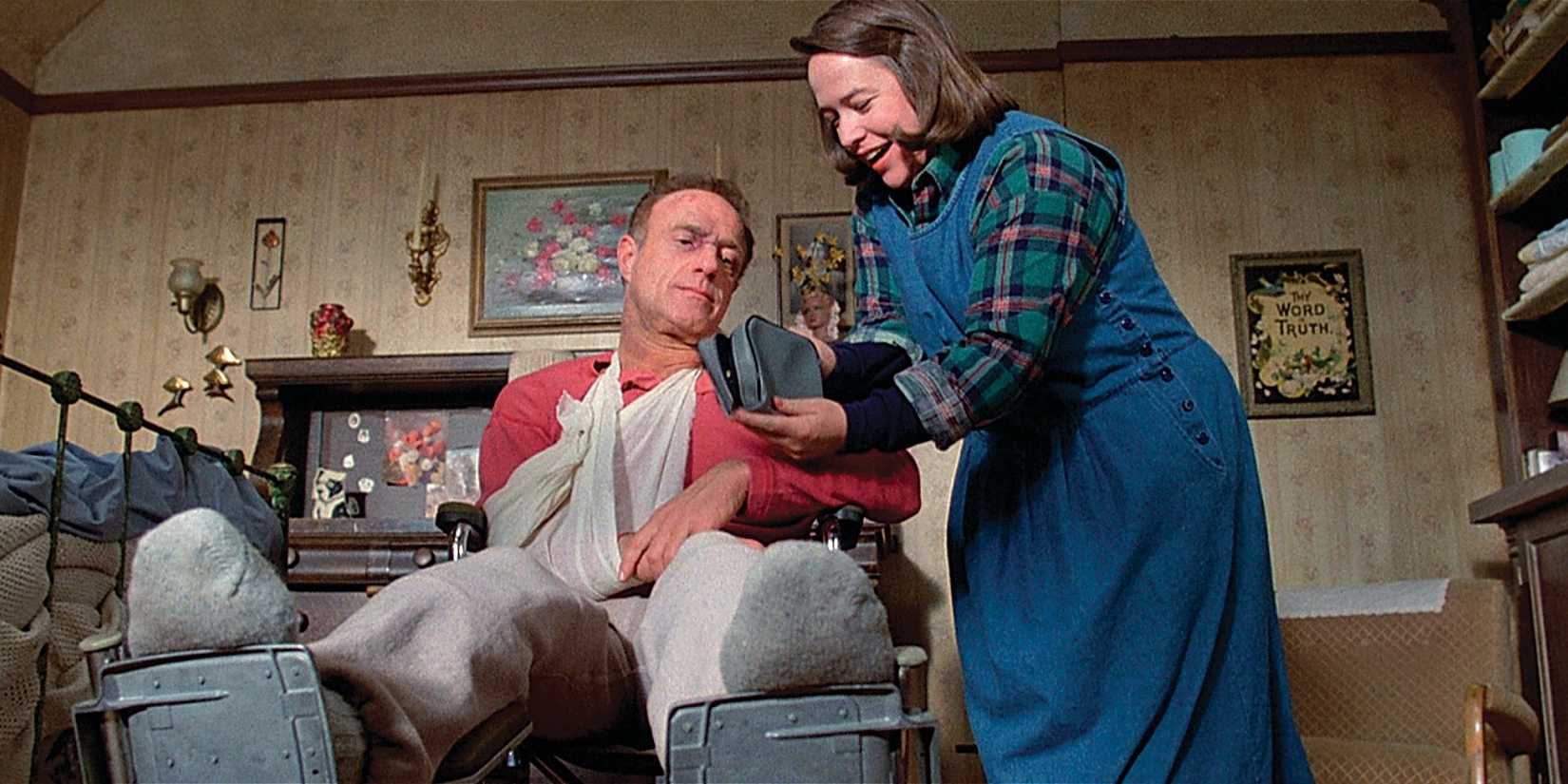 Annie shows something to Paul in a bag as he sits in a wheelchair injured in Misery