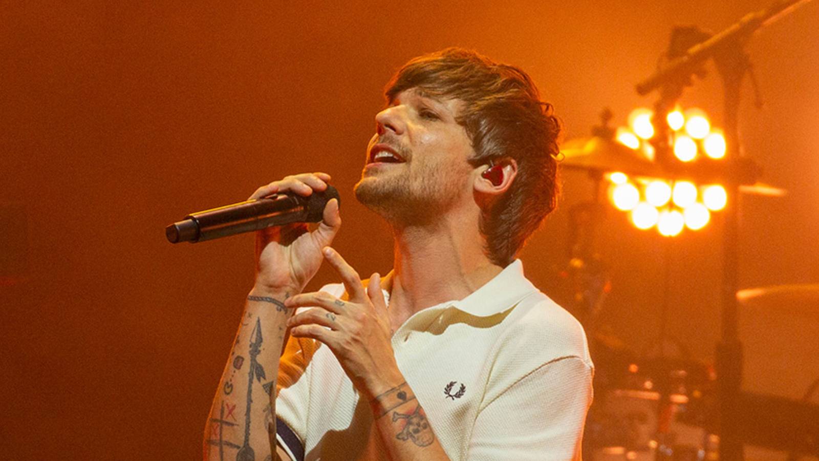 Louis Tomlinson singing into a microphone with an orange tint to the light