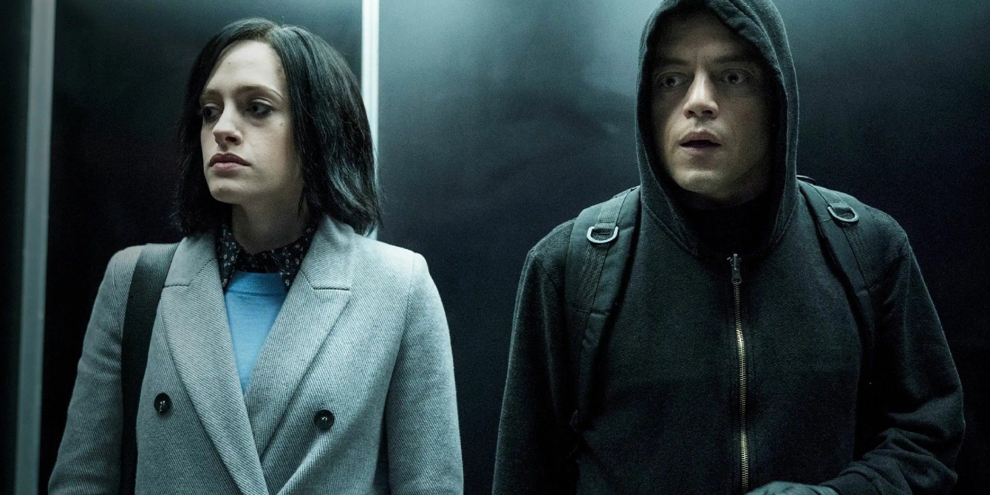 Darlene and Elliot in an elevator in Mr. Robot, with both looking worried, and Darlene wearing a black wig and business clothes, and Elliot wearing his black sweatshirt with the hood up