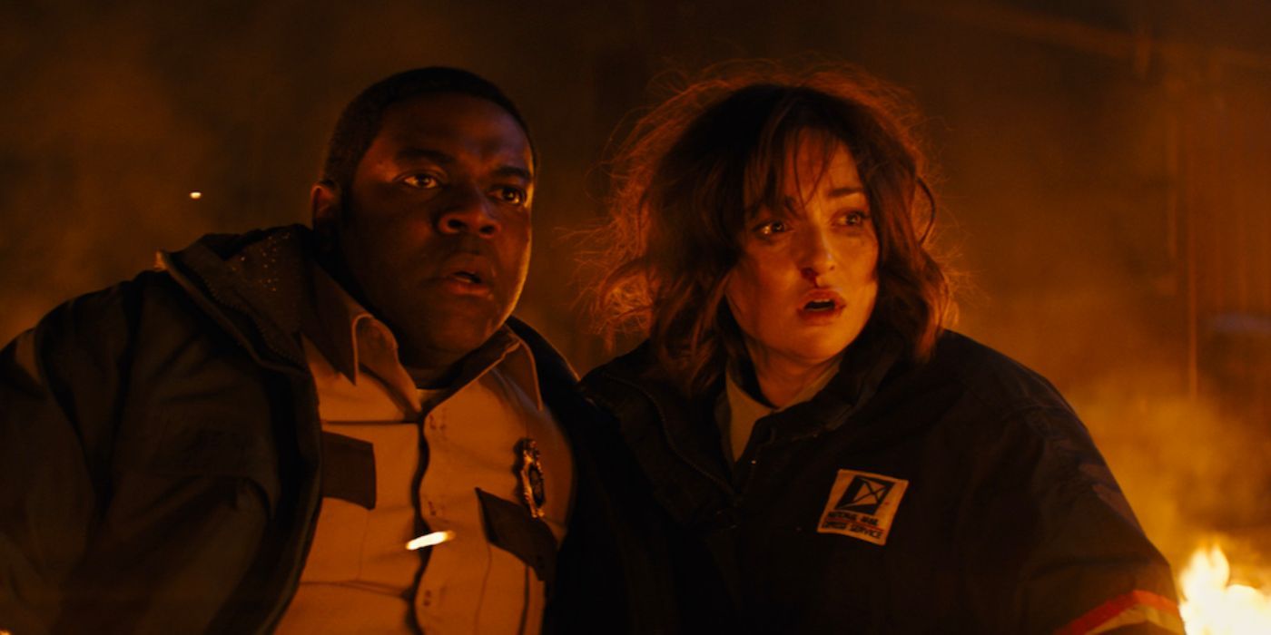 Sam Richardson and Milana Vayntrub looking scared outside among flames in Werewolves Within