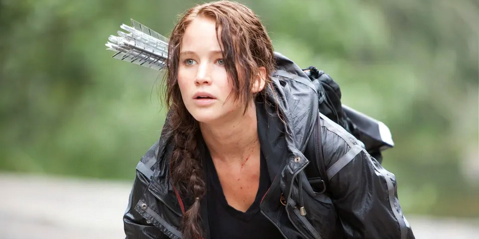 Katniss ajoelhada no chão, com flechas nas costas em Jogos Vorazes.