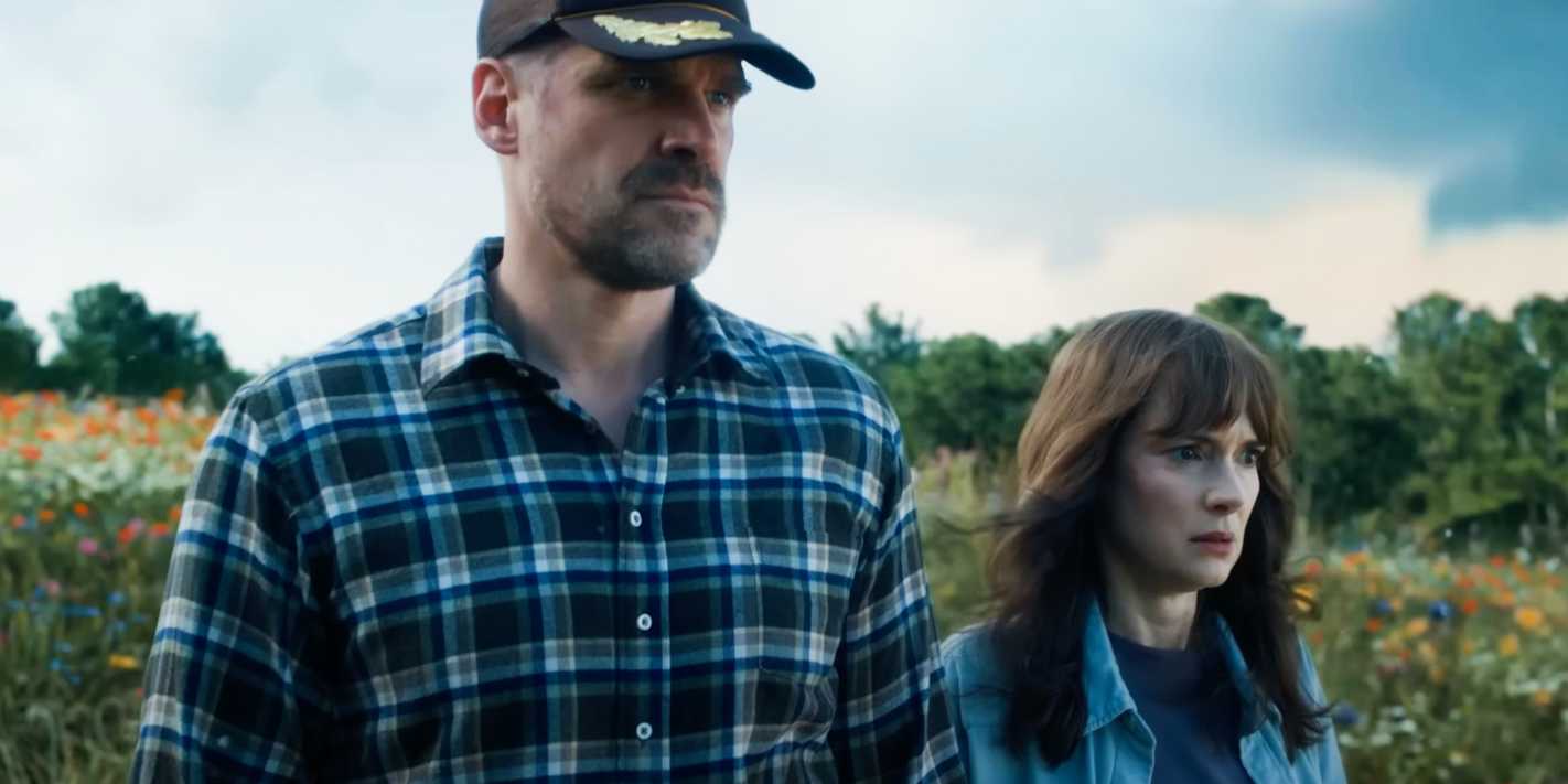 Jim Hopper (David Harbour) and Joyce Byers (Winona Ryder) looking on while standing in a field in Stranger Things season 4's final scene