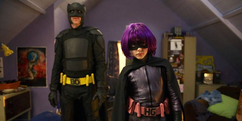 Big Daddy (Nicolas Cage) standing behind Hit-Girl (Chloë Grace Moretz) who is trying out her purple suit in Kick-Ass