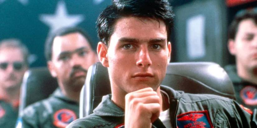Maverick (Tom Cruise) looks at the camera with other pilots sitting behind him in Top Gun (1986).