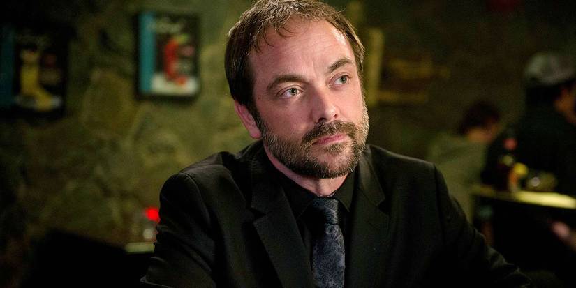 Crowley (Mark Sheppard) sitting at a table in Supernatural.