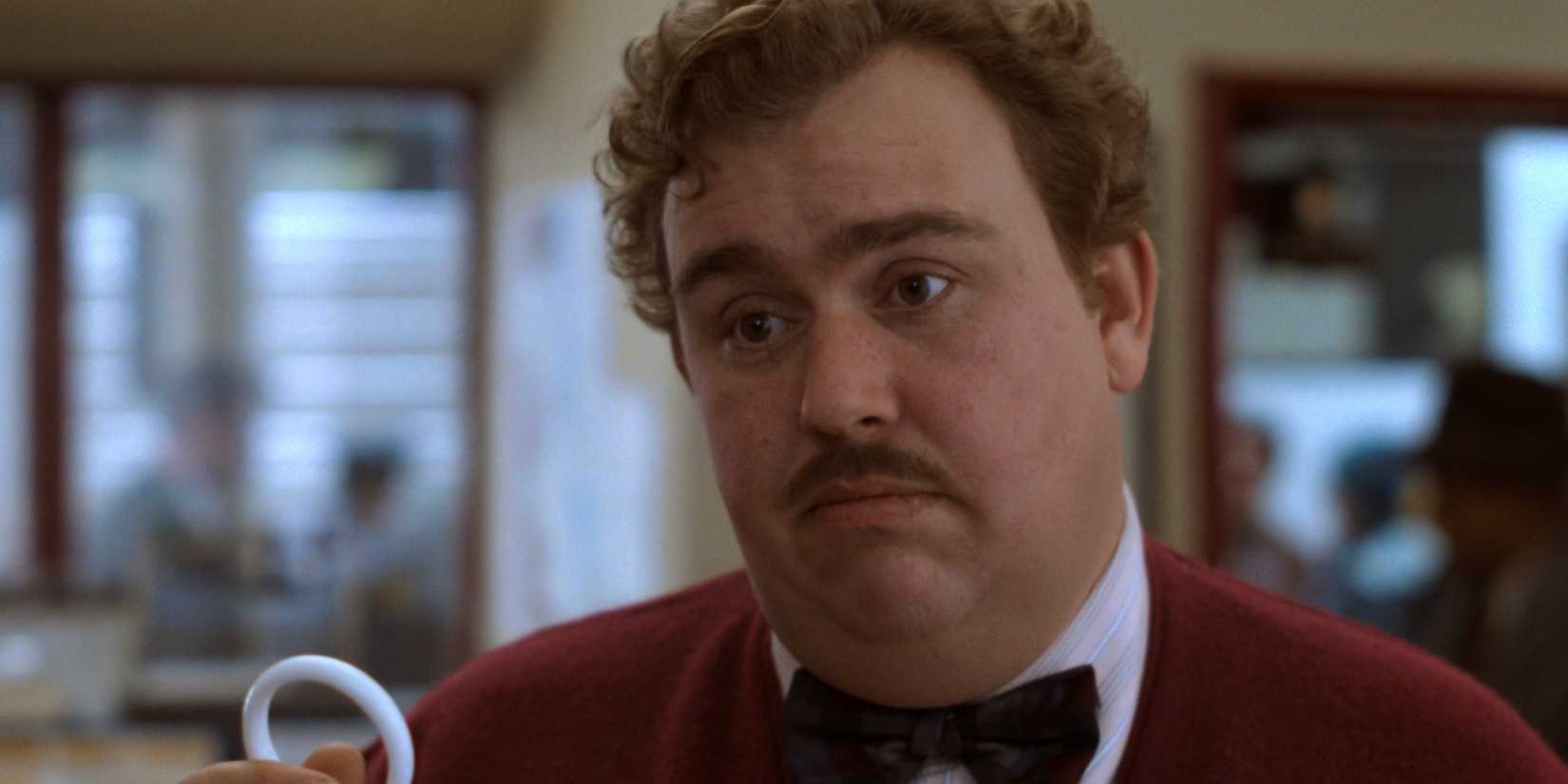 John Candy holding a single shower curtain ring in his hand in Planes Trains and Automobiles