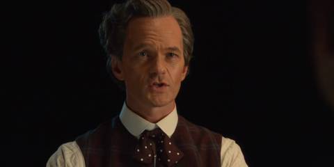 Neil Patrick Harris as the Toymaker, waring a red waiscoast and red bow tie with white spots, speaking to the Doctor in Doctor Who episode The Giggle