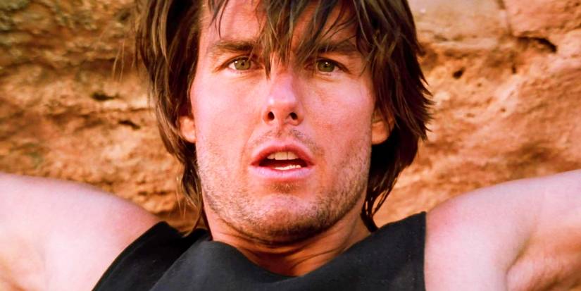 Tom Cruise holding onto a cliff as Ethan Hunt in Mission Impossible 2