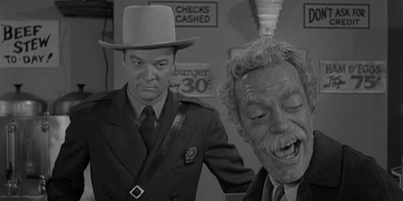 A still from the Will The Real Martian Please Stand Up? episode of The Twilight Zone showing a state trooper looking at a laughing man.