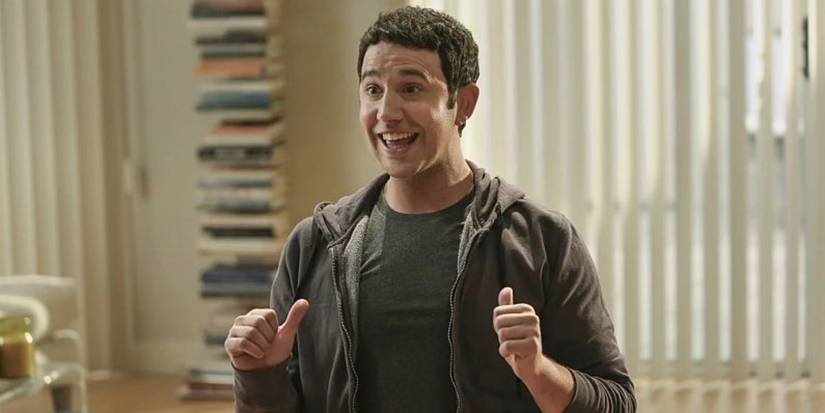Santino Fontana as Greg, smiling and pointing his thumbs at himself