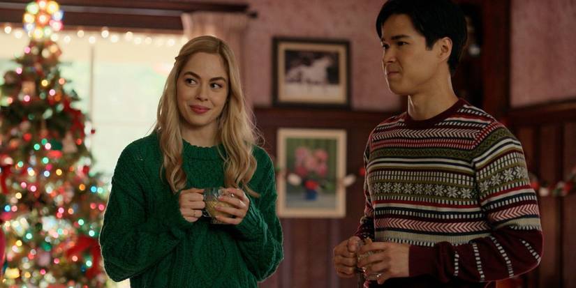 Lizzie and Denny wear holiday sweaters in front of the tree in Virgin River's Christmas episodes.