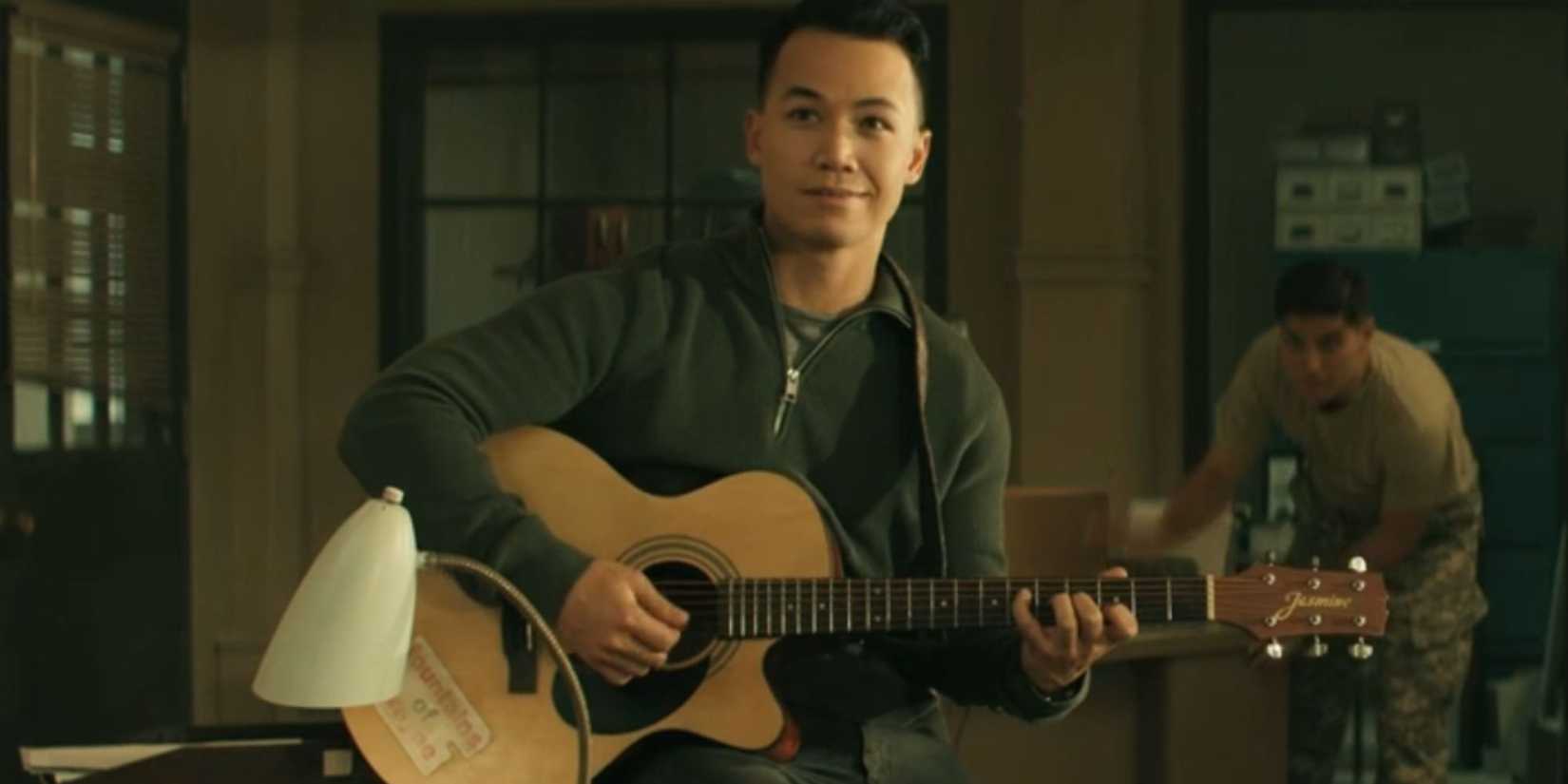 Shannon Kook as Tony Swan smiling and holding a guitar in Reacher