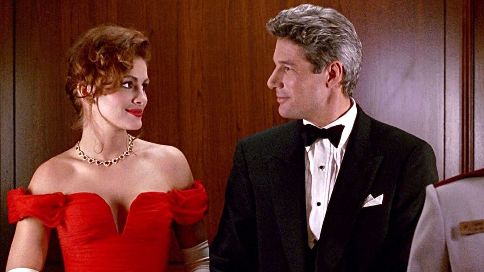 Richard Gere and Julia Roberts are dressed in formal attire and smile at each other in an elevator in Pretty Woman.  