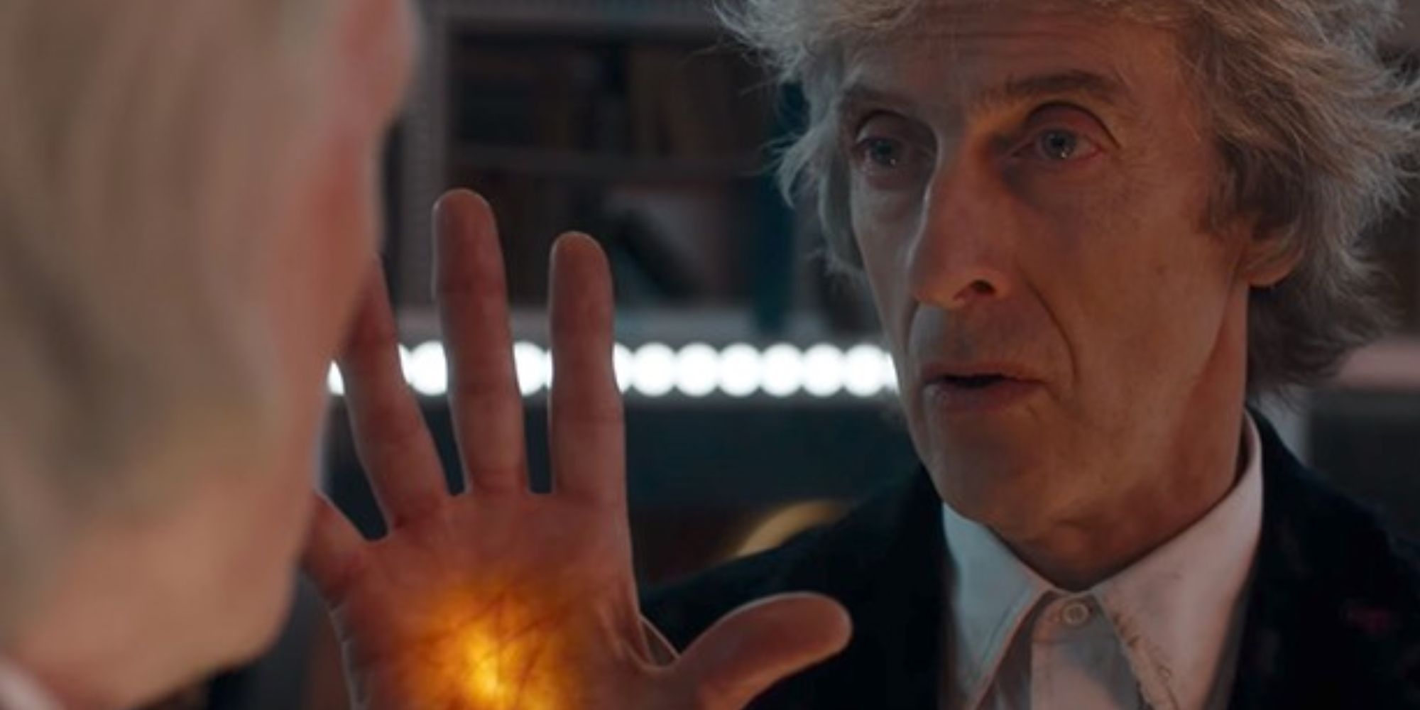 Peter Capaldi as the Twelfth Doctor showing his glowing palm to the First Doctor in Doctor Who