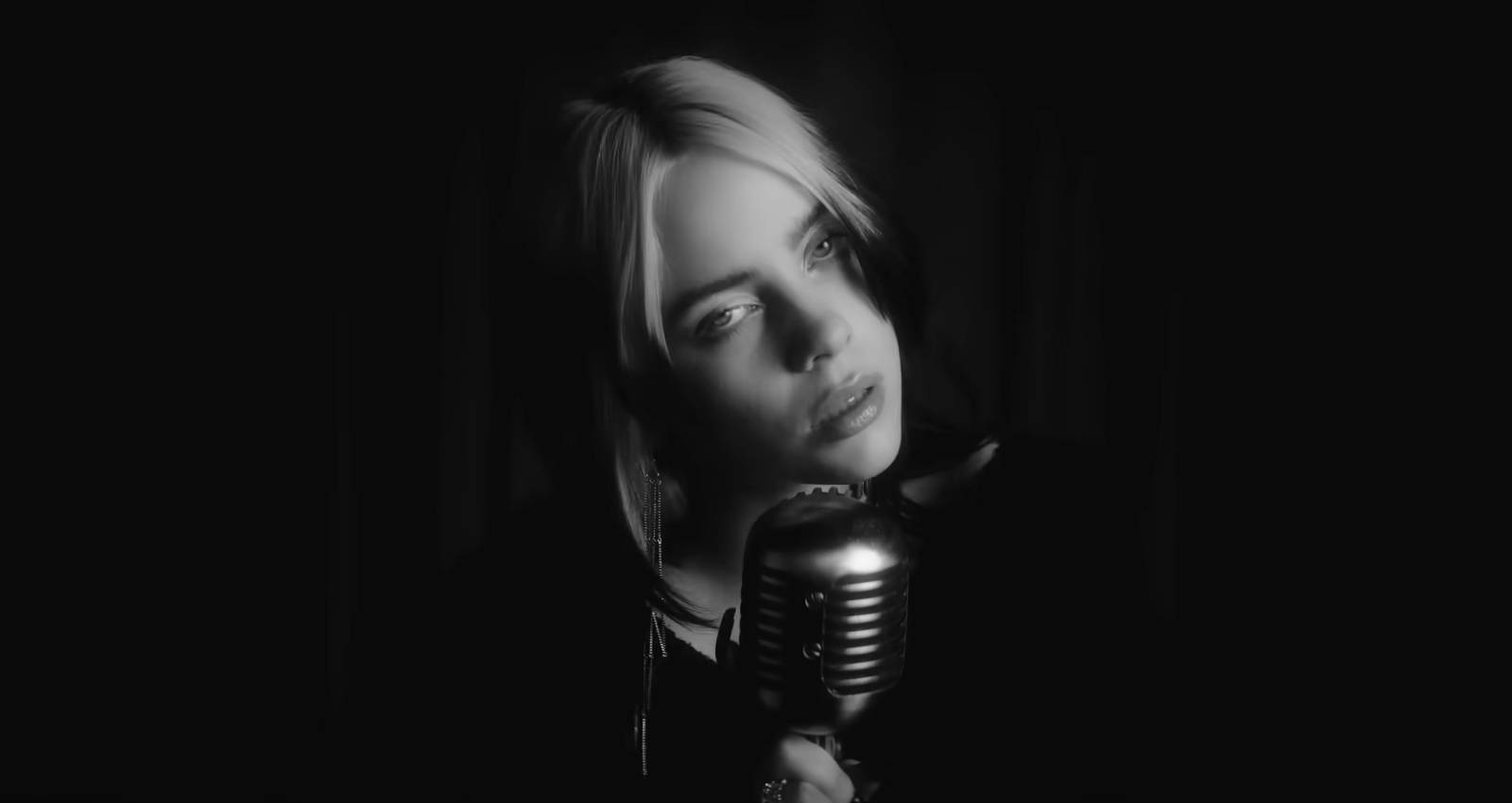 A black and white shot of Billie Eilish singing into an old school microphone in the official music video for 