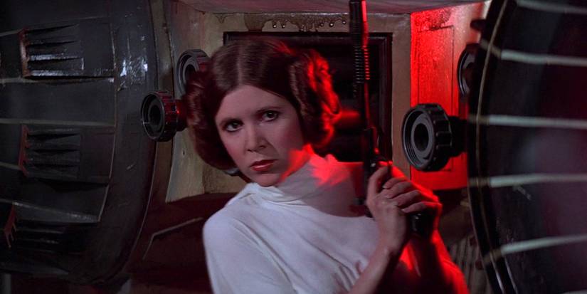Carrie Fisher as Princess Leia hides behind cover while holding a blaster in A New Hope