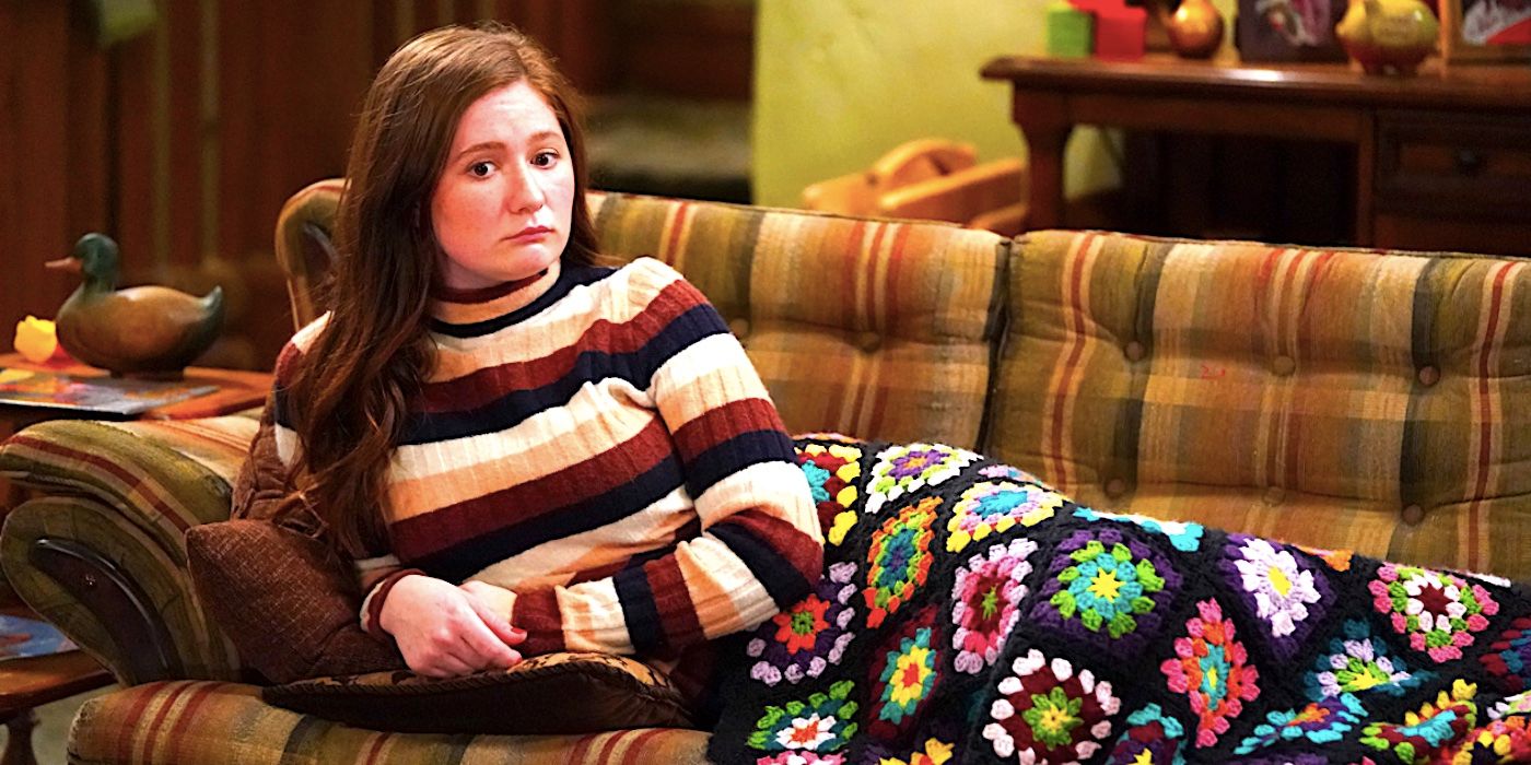 Emma Kenney's Harris lies on a couch covered by a quilt looking glum in The Conners season 3